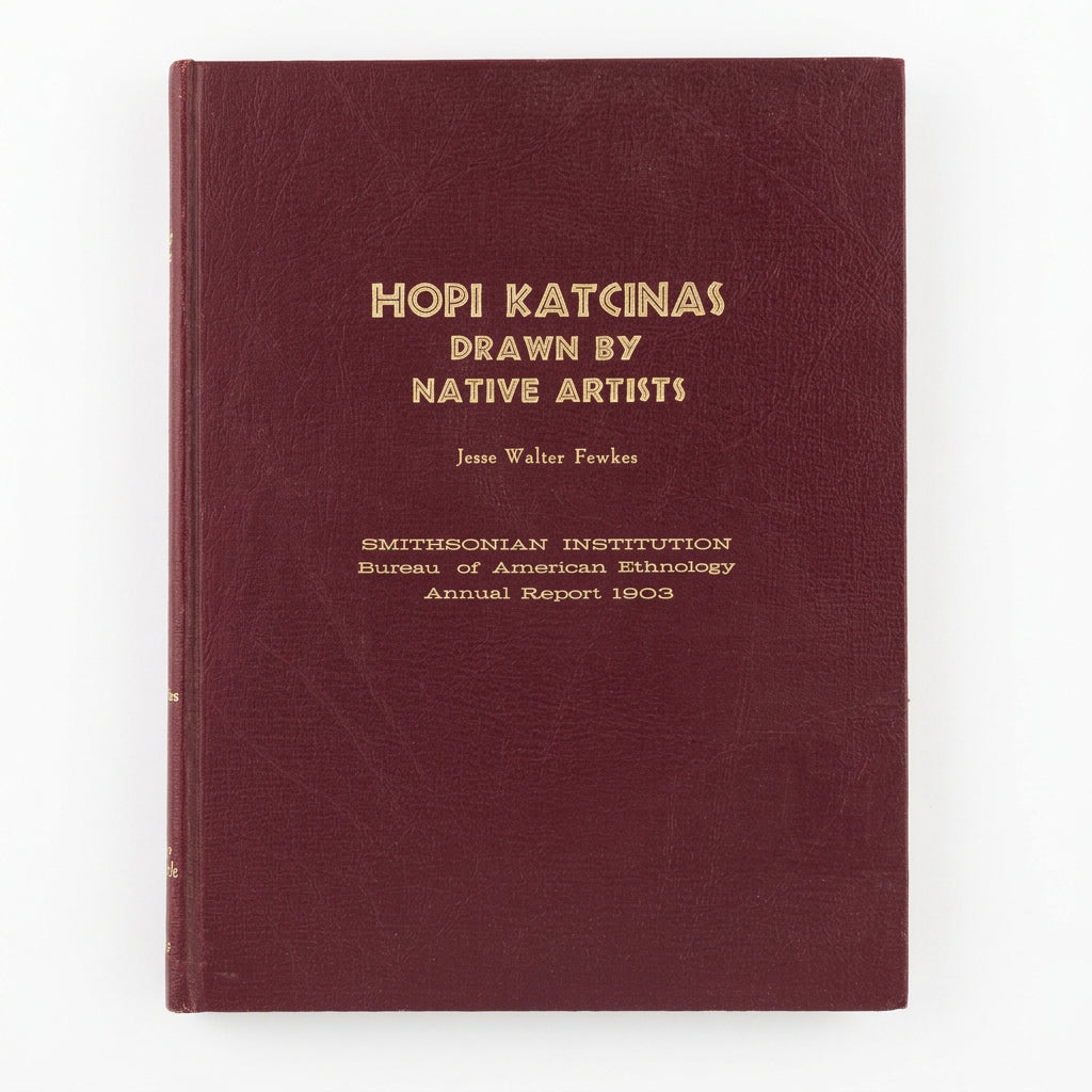 A vintage hardcover book titled 'HOPI KATCINAS DRAWN BY NATIVE ARTISTS' by Jesse Walter-Fewkes,  The book cover is a deep burgundy with gold lettering, placed on a light-colored wooden surface.